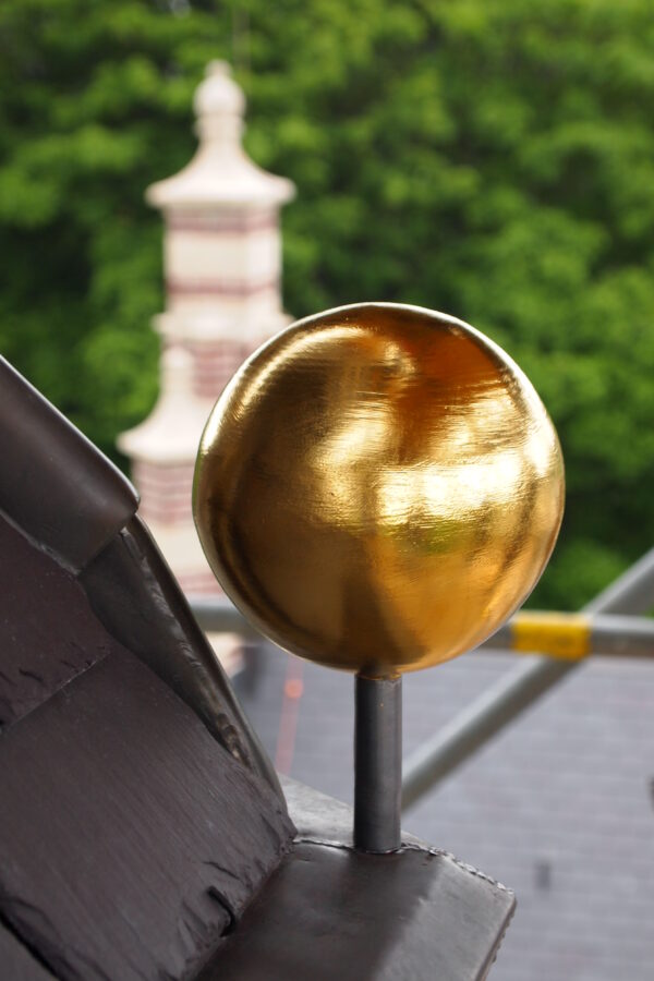 Close-up van een vergulde bol op pin als ornament op de hoek van een torenspits van Huize De Burgh in Eindhoven.